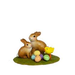 Two bunnies and a chick gather round a stack of colored Easter eggs