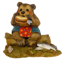 Large bear eats a fish sandwich sitting on a log